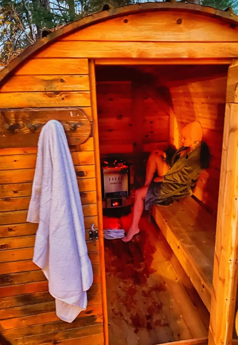 Personne se détendant dans le sauna tonneau illuminé avec une serviette suspendue à l’extérieur