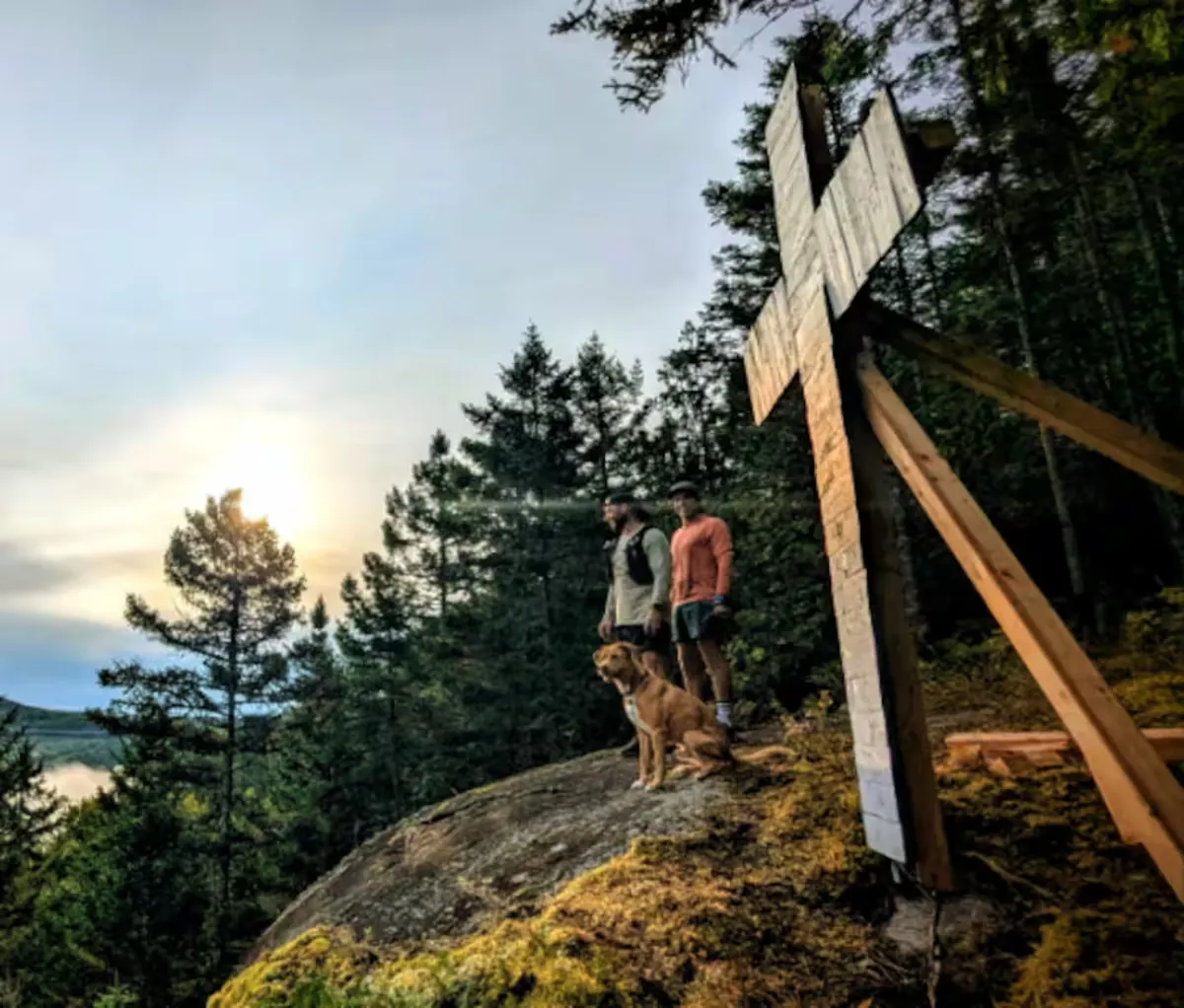 Deux randonneurs avec un chien au sommet, près d’une croix, au coucher du soleil